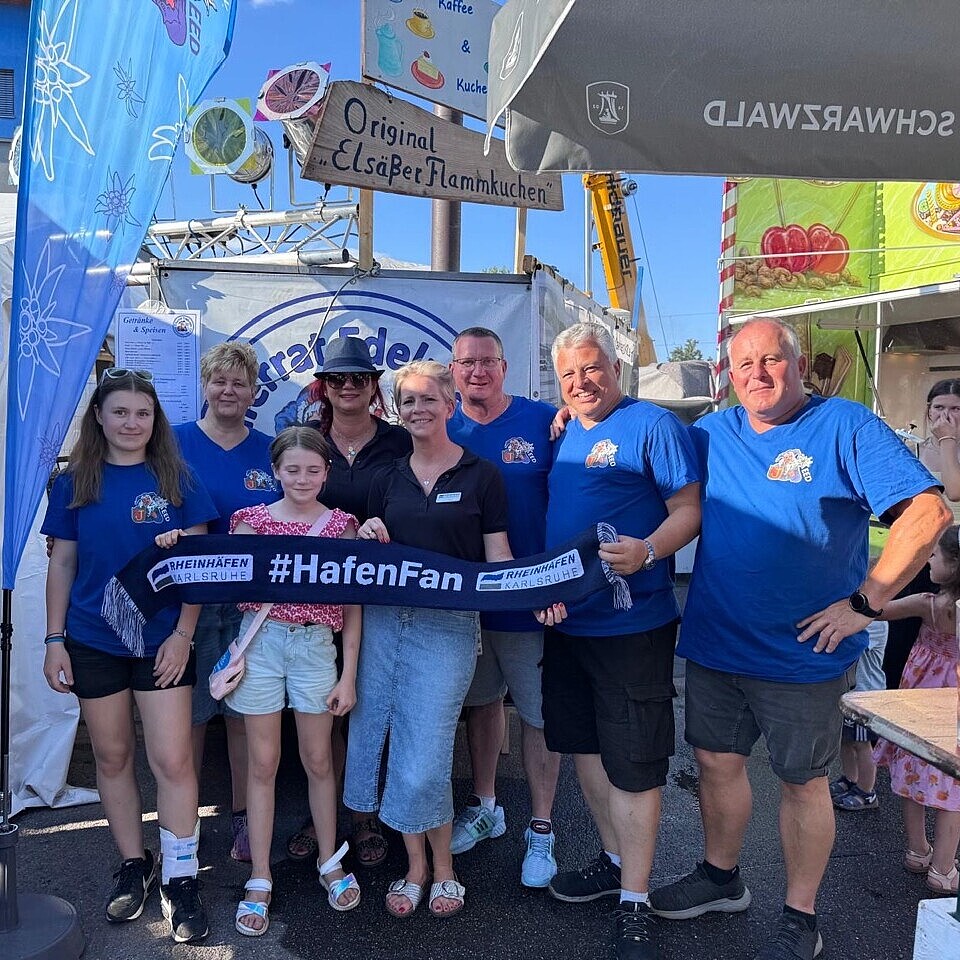 Besucherinnen und Besucher sowie die Mitarbeiterin Anna Mosur mit dem Hashtag #HafenFan beim HafenKulturFest am Karlsruher Rheinhafen, gemeinsames Gruppenfoto in sommerlicher Festivalatmosphäre.